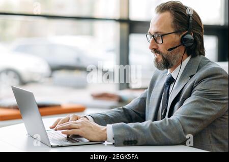 Concentrated middle aged businessman in headset is having a serious conversation, working on important project with colleagues. Focused male manager communicate with coworkers by video call Stock Photo