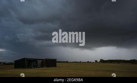 clouds over lone barn on dry meadow during thunderstorm and rain in summer Stock Photo