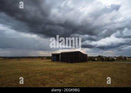 clouds over lone barn on dry meadow during thunderstorm and rain in summer Stock Photo