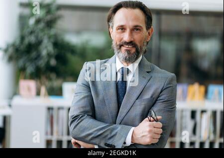 Formal portrait of senior elegant entrepreneur in stylish suit. Successful intelligent grey-haired businessman looks directly at the camera and friendly smiling Stock Photo