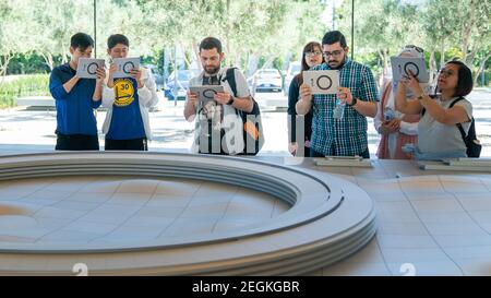 Cupertino, CA, USA - August 2019: Apple Store Cupertino with people looking at Infinite Loop Apple Headquarters through virtual reality using iPad tab Stock Photo