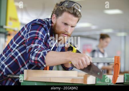 a man carpenter cuts a wooden beam using a handsaw Stock Photo