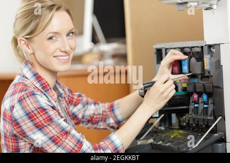 young woman changing ink cartridge on professional printer Stock Photo