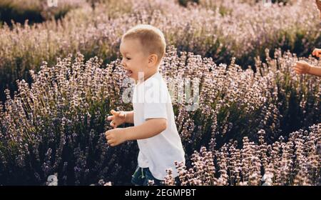 Charming caucasian small boy running through a lavender field smiling in a white shirt Stock Photo