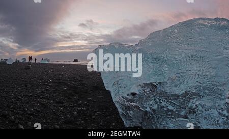 Big iceberg over black sand at at Diamond beach Iceland with people in the background nice sunrise colors Stock Photo