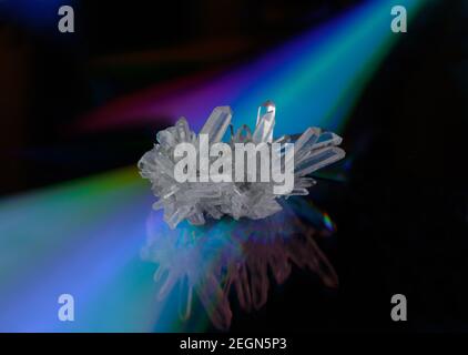 a cluster of raw clear quartz crystals on a reflective, iridescent background creating triangular gradients in green, blue, violet and red colors with Stock Photo