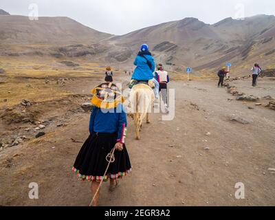 Peru, Vinicunca - October 1, 2019 - Tourists and locals walk on dirt road towards rainbow mountain, Stock Photo