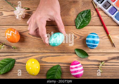 Hand is holding a cute green egg painted with colors next to other colorful eggs and fresh spring leaves. Easter and egg decorating concept Stock Photo