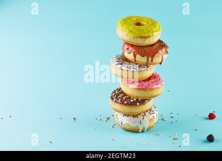 Multicolored donuts with icing and sprinkling stacked in a stack on a blue background. Stock Photo