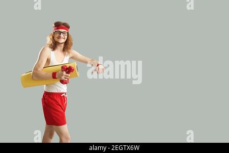 Cheerful hipster young man in red and white sportswear walking with dumbbels and skateboard Stock Photo