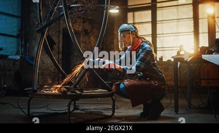 Young Contemporary Female Artist is Polishing a Metal Tube Sculpture with an Angle Grinder in a Studio Workshop. Pretty Empowering Woman. Stock Photo