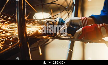 Close Up of Hands of a Metal Fabricator Wearing Safety Gloves and Grinding a Steel Tube Sculpture with an Angle Grinder in a Studio. Working with a Stock Photo