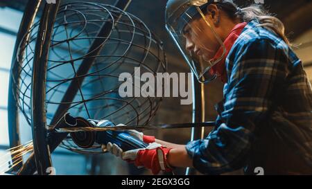 Close Up of Young Female Fabricator in Safety Mask. She is Grinding a Metal Tube Sculpture with an Angle Grinder in a Studio Workshop. Empowering Stock Photo