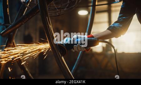 Close Up of Hands of a Metal Fabricator Wearing Safety Gloves and Grinding a Steel Tube Sculpture with an Angle Grinder in a Studio. Working with a Stock Photo