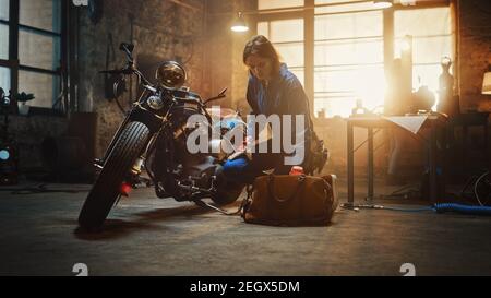 Young Beautiful Female Mechanic Comes Working on a Custom Motorcycle in Garage. Talented Girl Wearing a Blue Jumpsuit. She Looking for an Instrument
