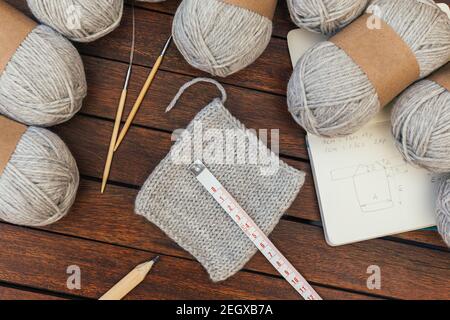 Top view of grey knitting yarns, needles on brown wooden background with scheme of sweater. Testing a wool with knitted piece Stock Photo