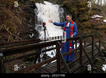 Rev Neil Glover, the minister at Aberfeldy Church in Perthshire, records a sermon beside the Birks of Aberfeldy waterfall - which once inspired Robert Burns to pen a poem. The clergyman has used lockdown to broadcast services in remote locations, describing being able to reach a worldwide audience as 'amazing'. Picture date: Thursday February 18, 2021. Stock Photo