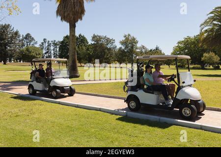 Two caucasian senior couples driving golf buggy on golf course talking and smiling Stock Photo