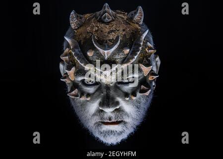 Devil demon. Head with thorns or warts, face covered with glitters, close up. Fantasy concept. Demon on serious face, black background. Stock Photo