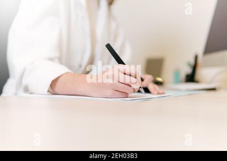 Close up of hands of female doctor writing a prescription at her office desk. Stock Photo