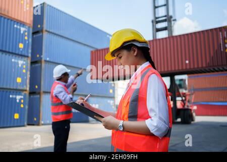 Asian worker woman is checking the container after the repair complete with foreman using walkie talkie to command crane lifting container in backgrou Stock Photo