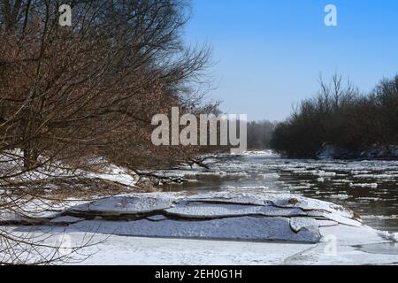 The river hung in winter, thaw by the river, trees by the shore, tree stump in the ice, snow and floe on the river Stock Photo