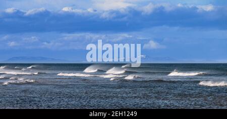 LOSSIEMOUTH BEACH MORAY COAST SCOTLAND WIND SWEPT WAVES WITH SPRAY OR WHITE HORSES AND SNOW COVERED HILLS OF SUTHERLAND Stock Photo