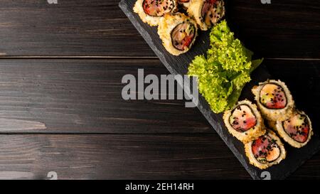 Custom sushi roll in tempura with nori, fresh salmon, tuna, avocado, masago caviar, drizzled with pineapple sauce with salad pouring as decoration on Stock Photo