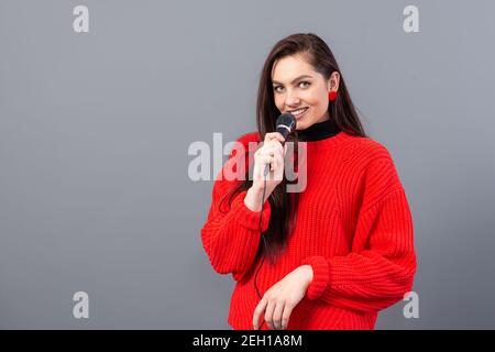 female conference speaker dressed in a red sweater during presentation calling for attention, isolated on grey Stock Photo