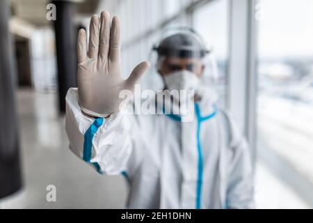 Medic man in a white hazmat suit and mask gesturing stop with hand in the clinic Stock Photo