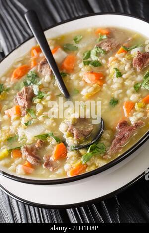 Scotch broth is a traditional Scottish soup made from lamb, and vegetables, barley, peas closeup in the plate on the table. Vertical Stock Photo