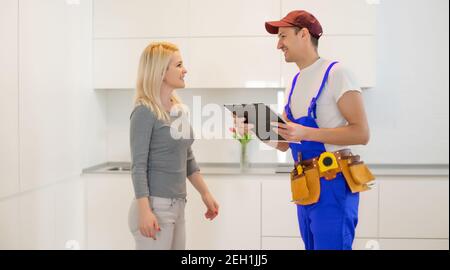Young Woman Looking At Male Technician Checking Dishwasher In Kitchen Stock Photo