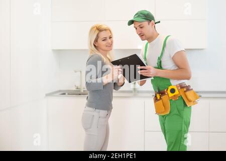 Young Woman Looking At Male Technician Checking Dishwasher In Kitchen Stock Photo