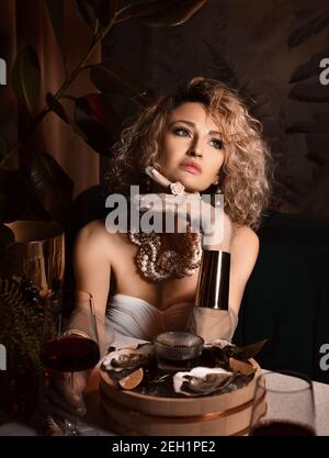 Portrait of pensive beautiful blonde curly hair woman sitting in seafood restaurant eating oysters and drink wine Stock Photo