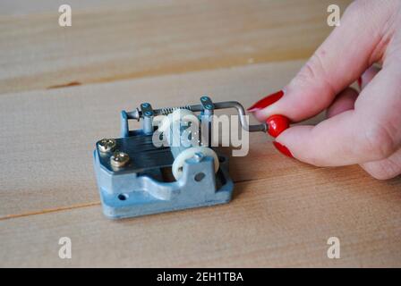 Closeup female hand holding a vintage mechanical music box with red handle on wooden plank. Put music box on wooden surface to obtain maximum sound Stock Photo