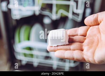 Selective focus on woman hand, holding homemade natural dishwasher pod defocus dishes in dishwasher on background. Green sustainable lifestyle concept Stock Photo