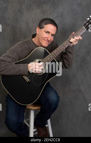 man sitting on stool playing acoustic steel stringed guitar Stock Photo