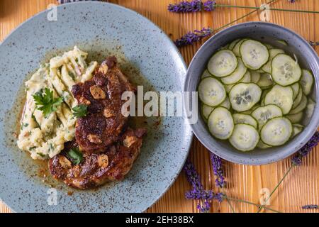 Baked pork neck with mashed potatoes with parsley and roasted bacon and cucumber salad. Stock Photo