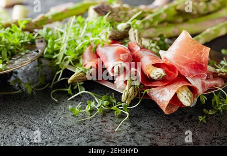 Asparagus wrapped in prosciutto with cress salad on a grey background. Stock Photo