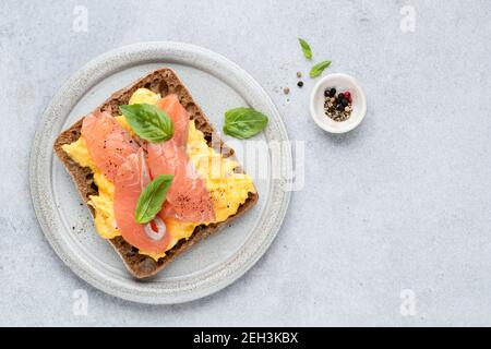 Scrambled eggs and smoked salmon on rye bread toast. Top view. Healthy breakfast or lunch sandwich. Grey concrete background, copy space Stock Photo