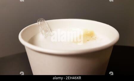 Milk coffee in paper white glass from vending coffee machine with plastic spoon stirrer close-up Stock Photo