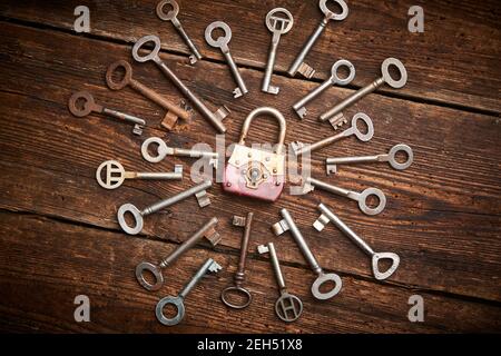 Vintage rusty padlock surrounded by group of old keys on a weathered wooden background. Internet security and data protection concept, blockchain and Stock Photo