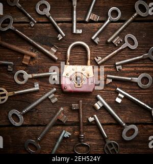Vintage rusty padlock surrounded by group of old keys on a weathered wooden background. Internet security and data protection concept, blockchain and Stock Photo