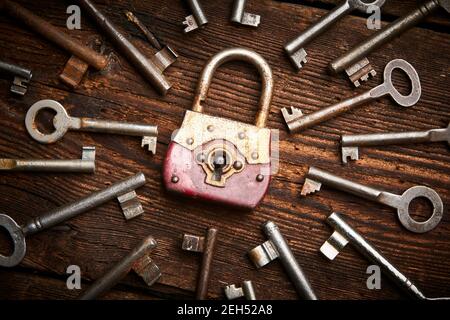 Vintage rusty padlock surrounded by group of old keys on a weathered wooden background. Internet security and data protection concept, blockchain and Stock Photo