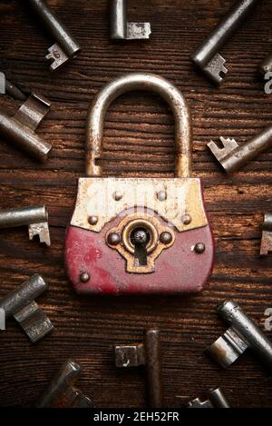 Vintage rusty padlock surrounded by group of old keys on a weathered wooden background. Internet security and data protection concept, blockchain and Stock Photo