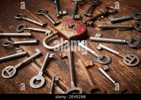 Vintage rusty padlock surrounded by group of old keys on a weathered wooden background. Internet security and data protection concept, blockchain and Stock Photo