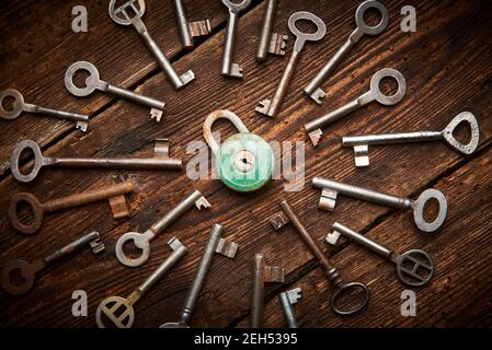 Vintage rusty padlock surrounded by group of old keys on a weathered wooden background. Internet security and data protection concept, blockchain and Stock Photo