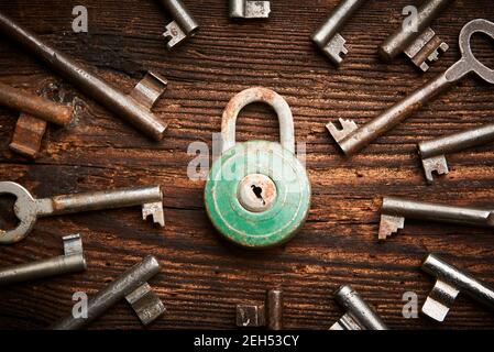 Vintage rusty padlock surrounded by group of old keys on a weathered wooden background. Internet security and data protection concept, blockchain and Stock Photo