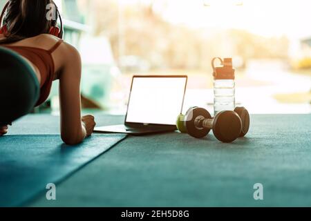 Full-length of young beautiful woman in sportswear doing plank at gym. Women and ear phone listen music between workout. Stock Photo