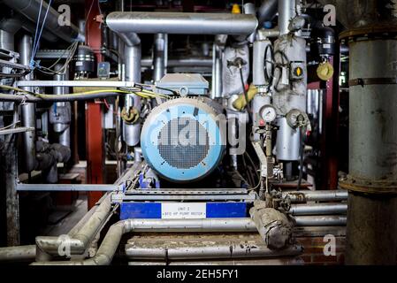 Large blue metal electric water pump turbine motor in industrial power station setting surrounded by steel pipes pressure gauges and electrical wires Stock Photo